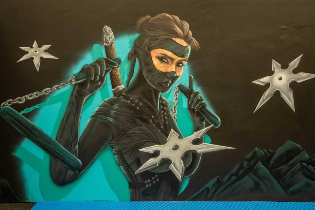 Vibrant street art mural of a female ninja with weapons at Blackbook Ink.